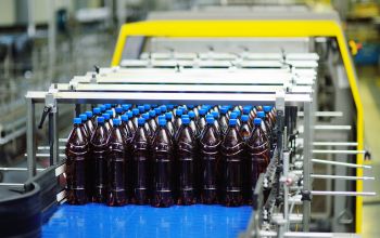 Conveyor belt in a beverage factory with rows of sealed brown bottles, representing automated bottling processes enabled by solenoid valve systems