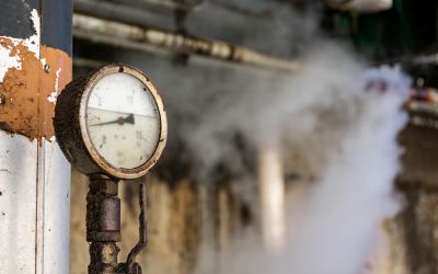 Pressure gauge indicating high steam pressure in a food processing facility with visible steam release for safety.