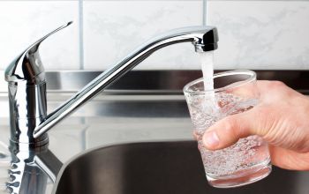 Glass being filled with purified water from kitchen tap, representing clean water solutions in water treatment and management systems